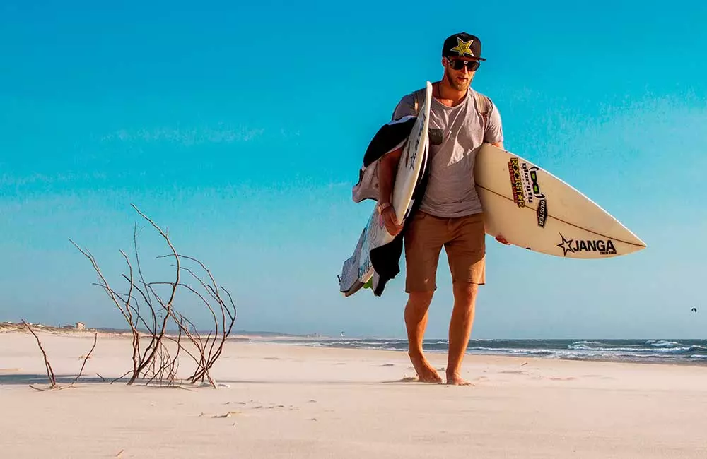 Surfer mit Brett unter dem Arm läuft am sonnigen Strand entlang